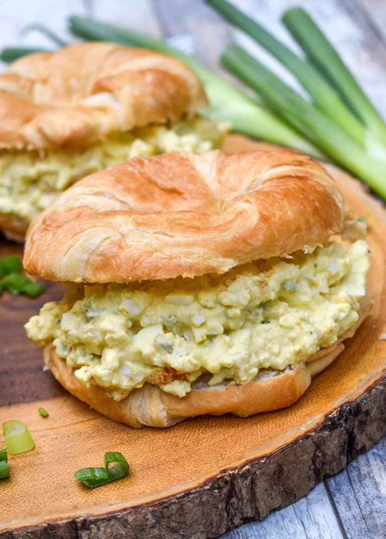 deviled egg salad on croissant rolls resting on a wooden cutting board