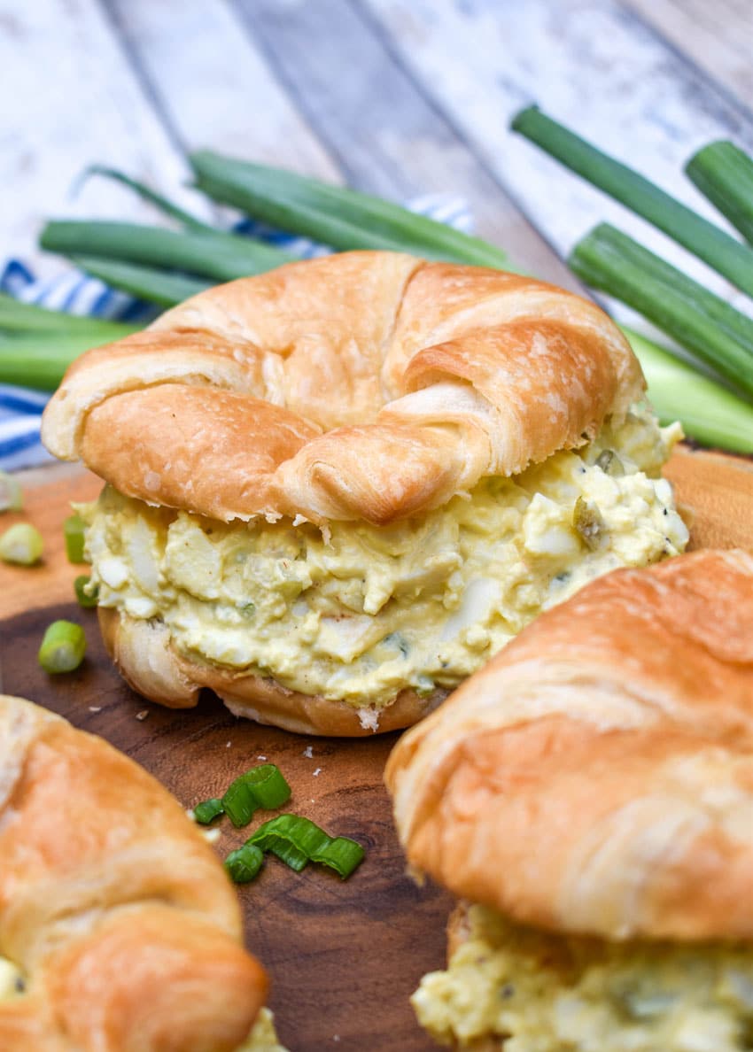 deviled egg salad on croissant rolls resting on a wooden cutting board