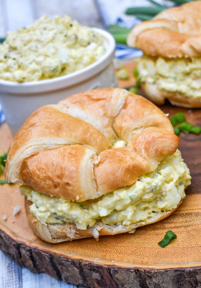 deviled egg salad on croissant rolls resting on a wooden cutting board