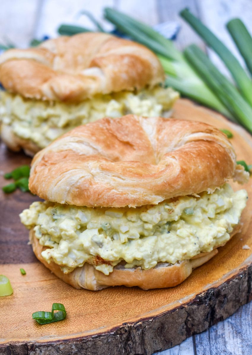 deviled egg salad on croissant rolls resting on a wooden cutting board