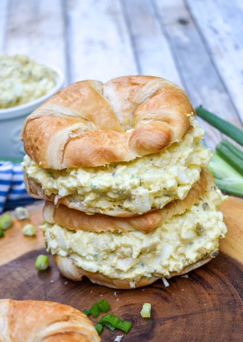 deviled egg salad on croissant rolls resting on a wooden cutting board