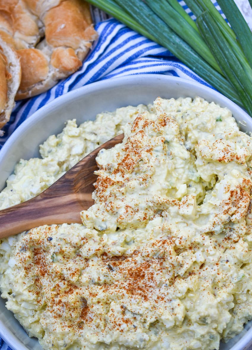 a wooden spoon scooping deviled egg salad out of a shallow white serving bowl