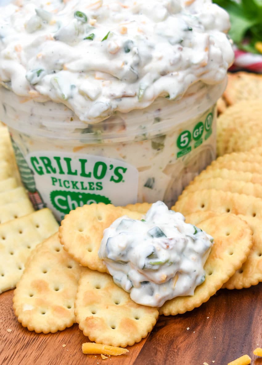 a cracker topped with creamy dill pickle dip resting on a wooden cutting board