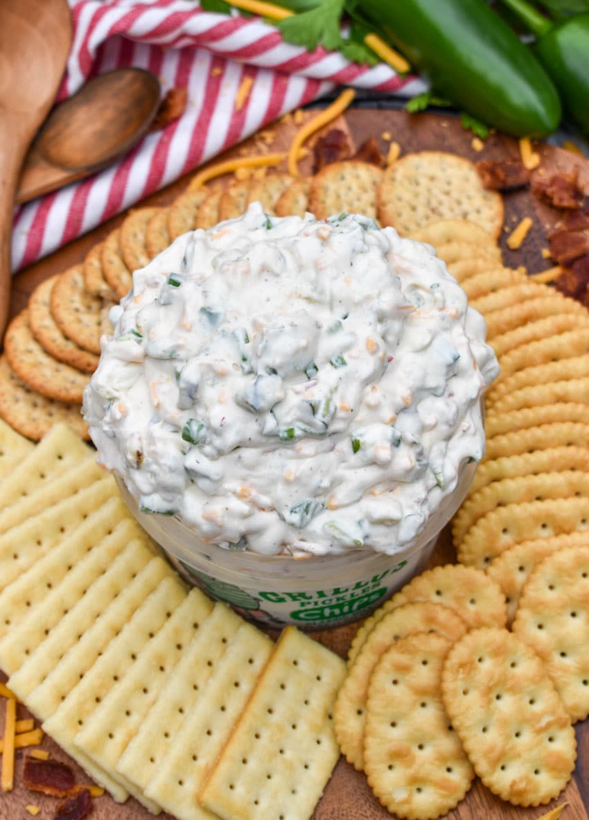 a plastic tub filled with grillo's dill pickle dip surrounded by crackers