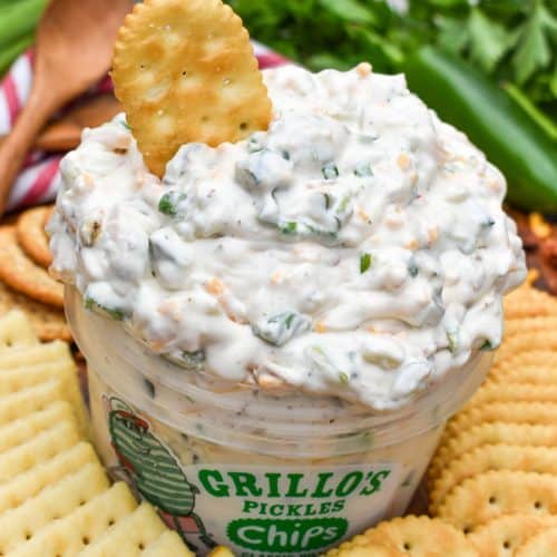 a plastic tub filled with grillo's dill pickle dip surrounded by crackers