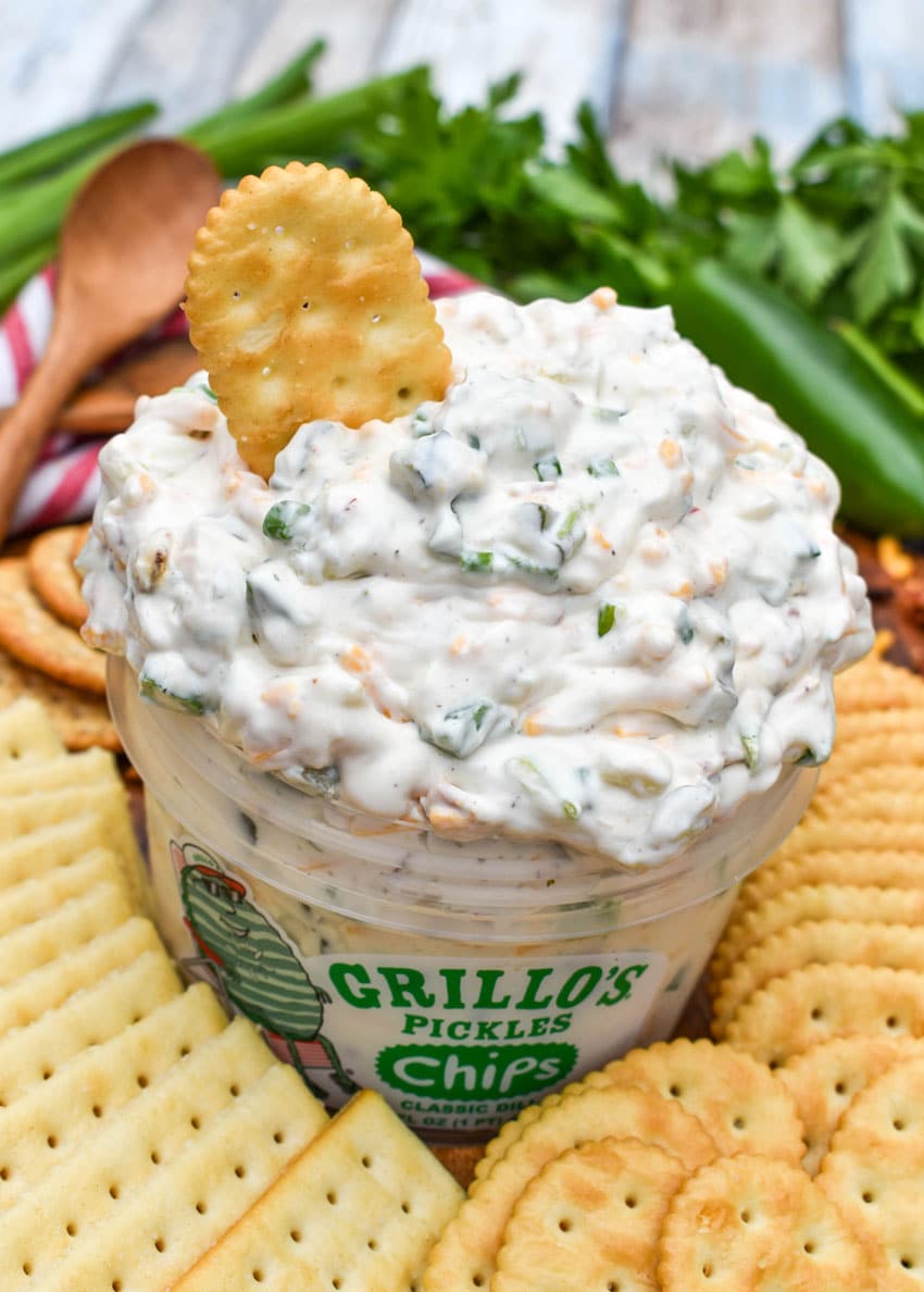 a plastic tub filled with grillo's dill pickle dip surrounded by crackers