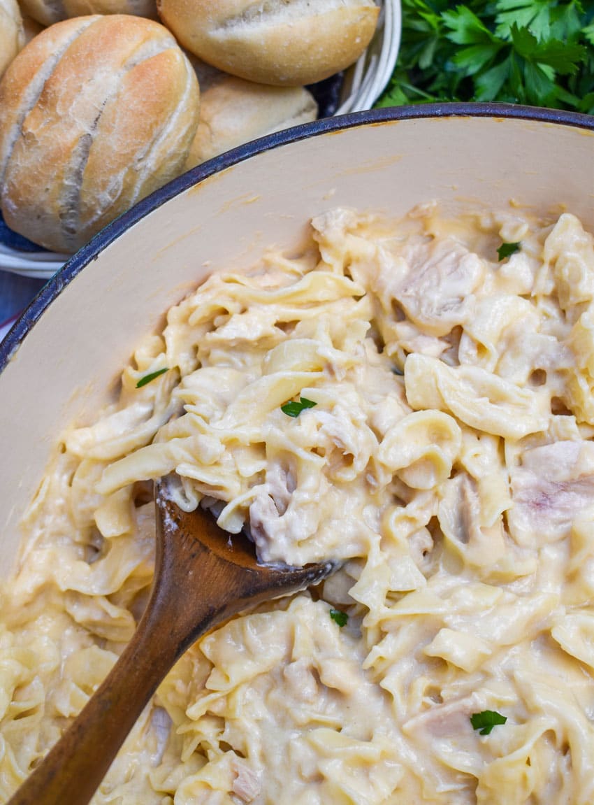 a wooden spoon scooping a homemade tuna helper recipe out of a large cast iron pot