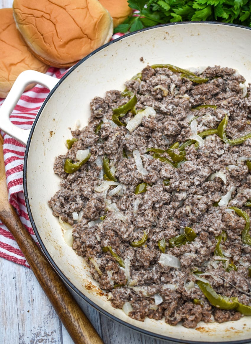 cheesy ground beef with sauteed green peppers and onions in a cast iron skillet