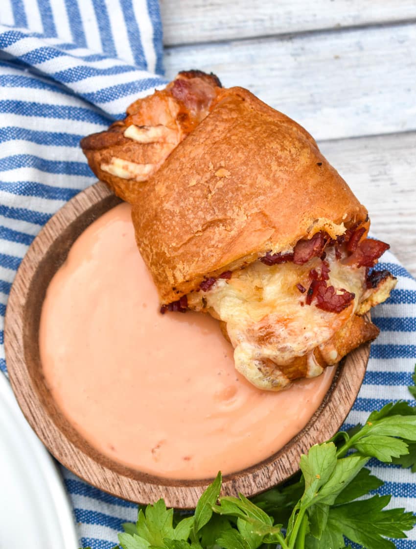 a baked reuben crescent roll resting on the edge of a small wooden bowl filled with thousand island dressing