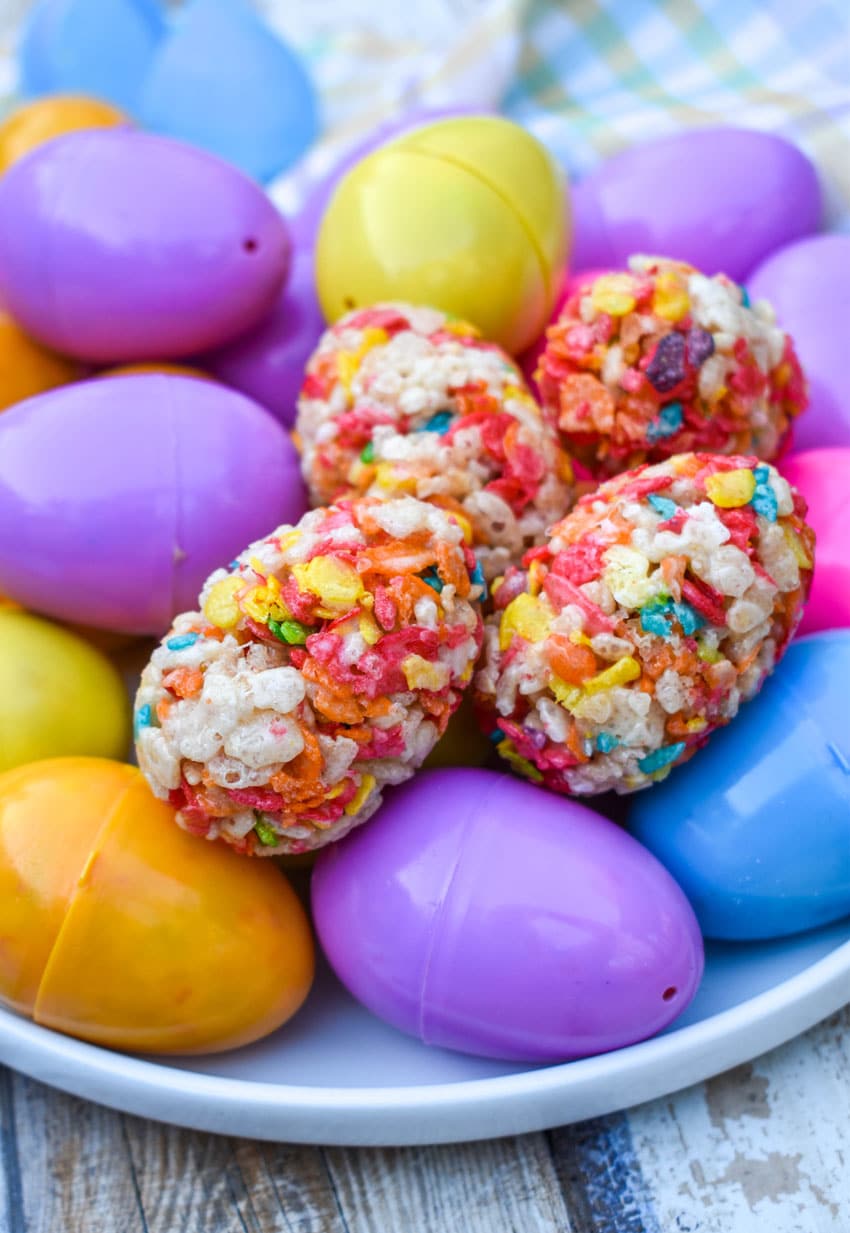 Rice Krispie Treats Easter Eggs resting on top of colorful plastic eggs on a white plate