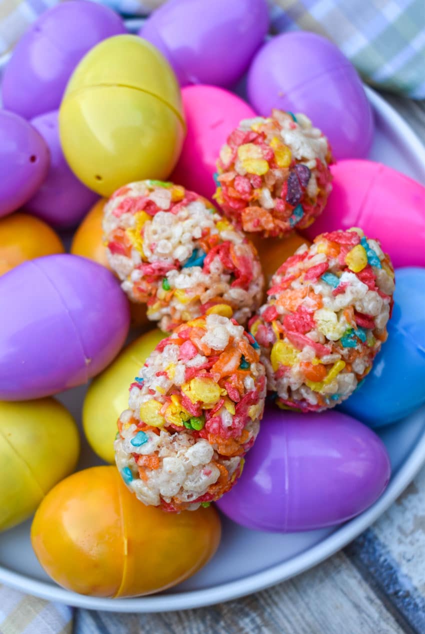 Rice Krispie Treats Easter Eggs resting on top of colorful plastic eggs on a white plate