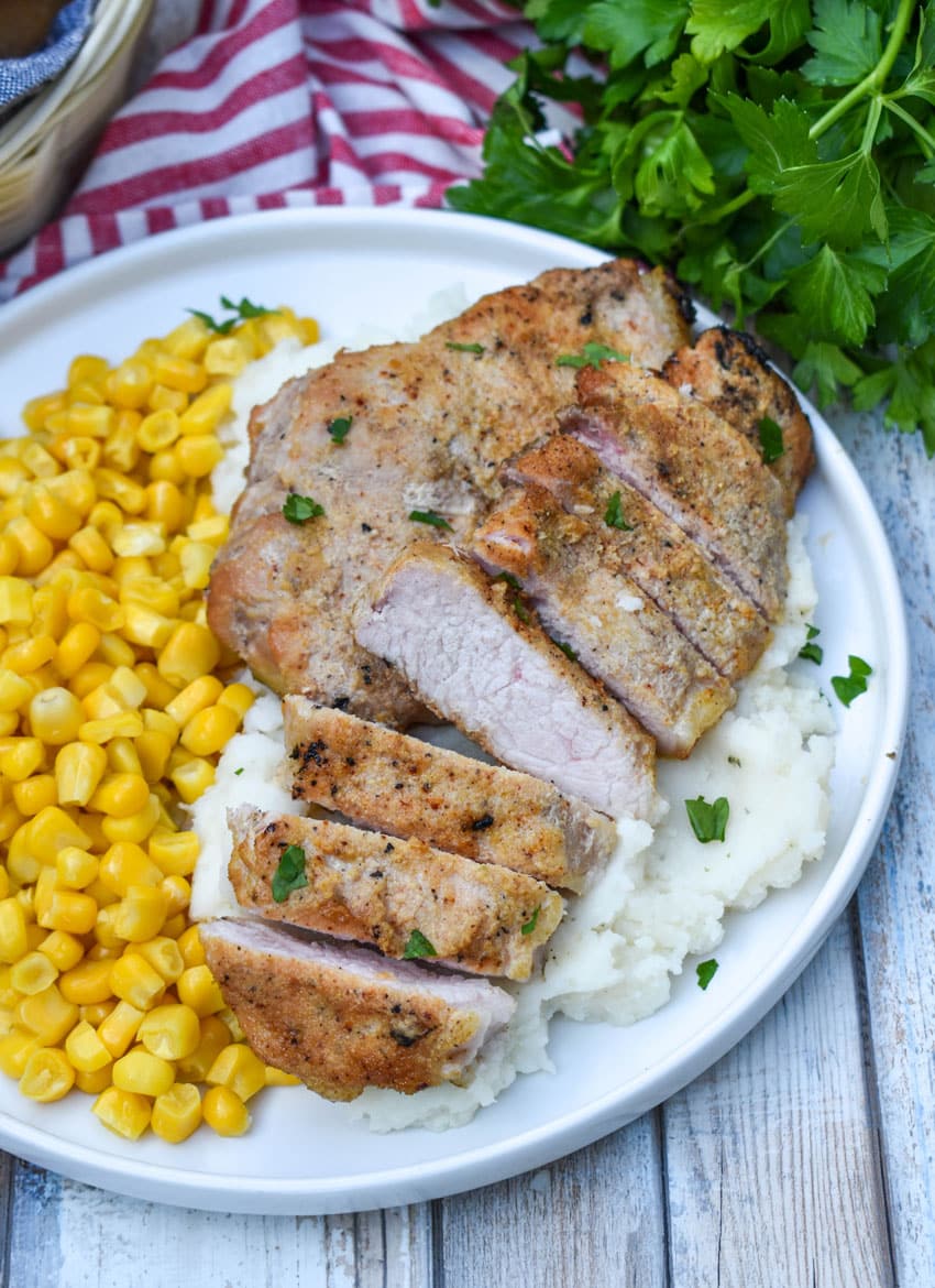 smoked pork chops over mashed potatoes next to corn kernels on a white plate