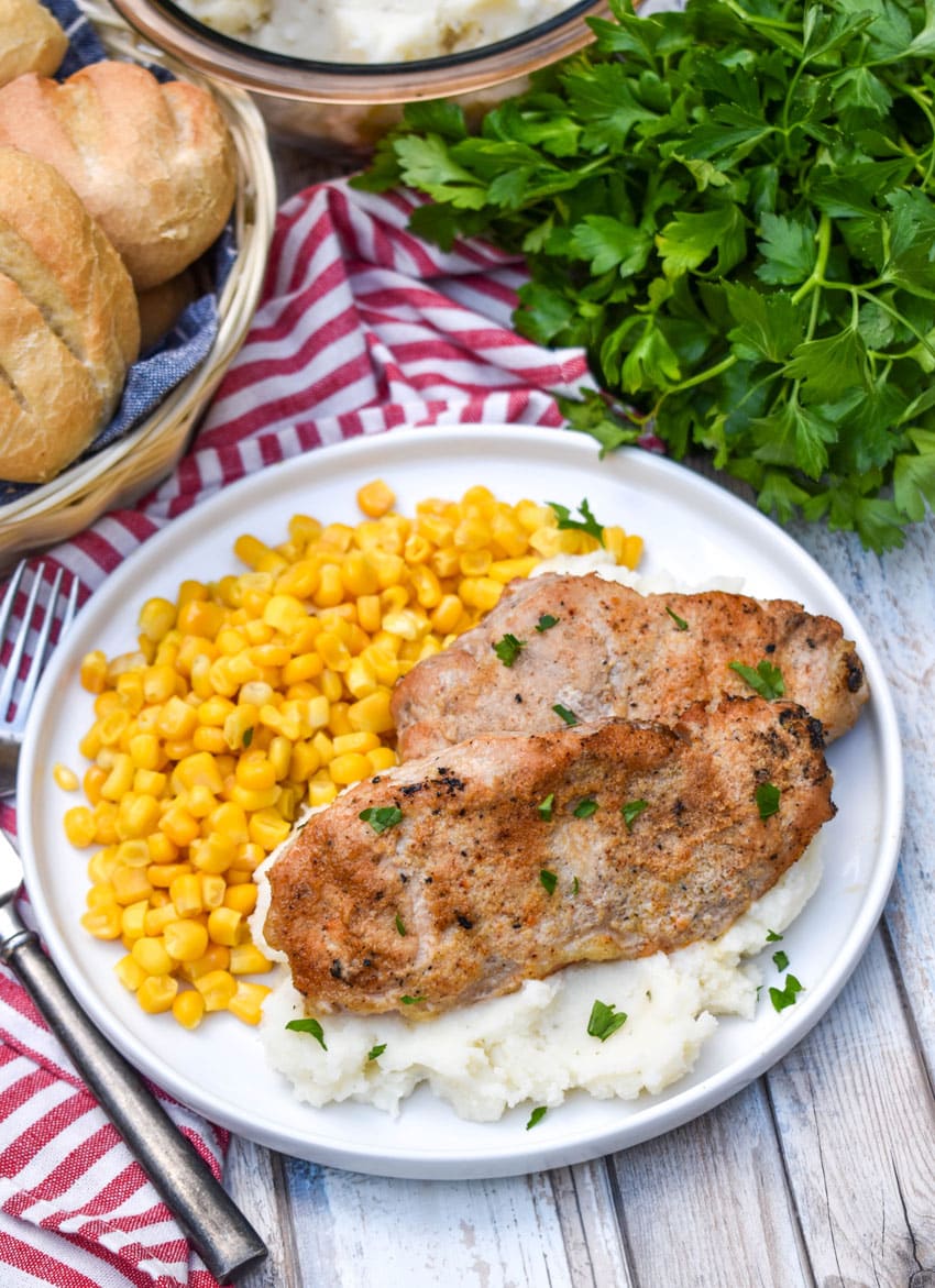 smoked pork chops over mashed potatoes next to corn kernels on a white plate
