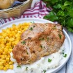 smoked pork chops over mashed potatoes next to corn kernels on a white plate