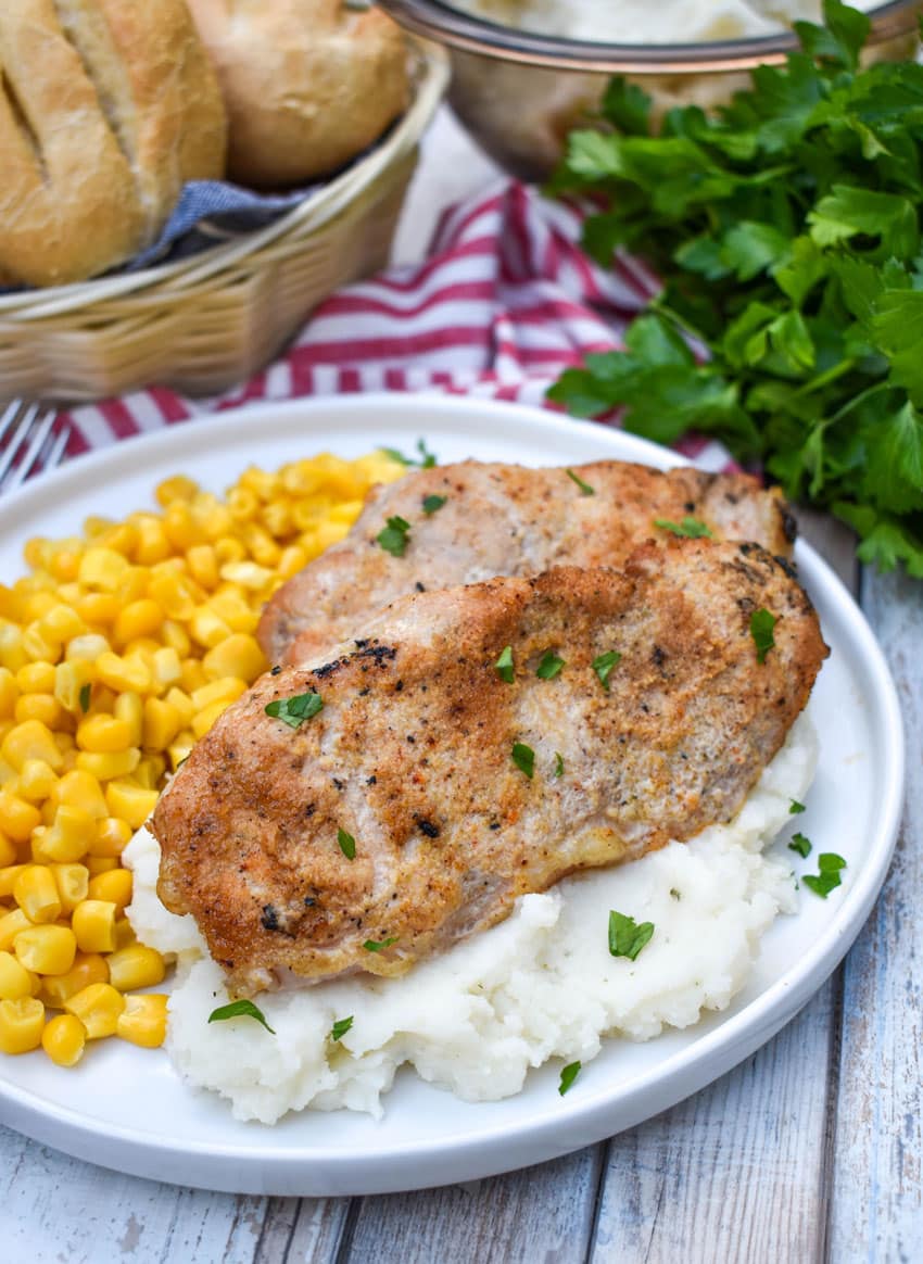 smoked pork chops over mashed potatoes next to corn kernels on a white plate