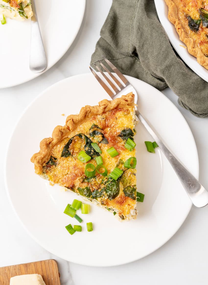 a slice of crab quiche on a small white plate with a silver fork resting on the side