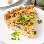 a slice of crab quiche on a small white plate with a silver fork resting on the side