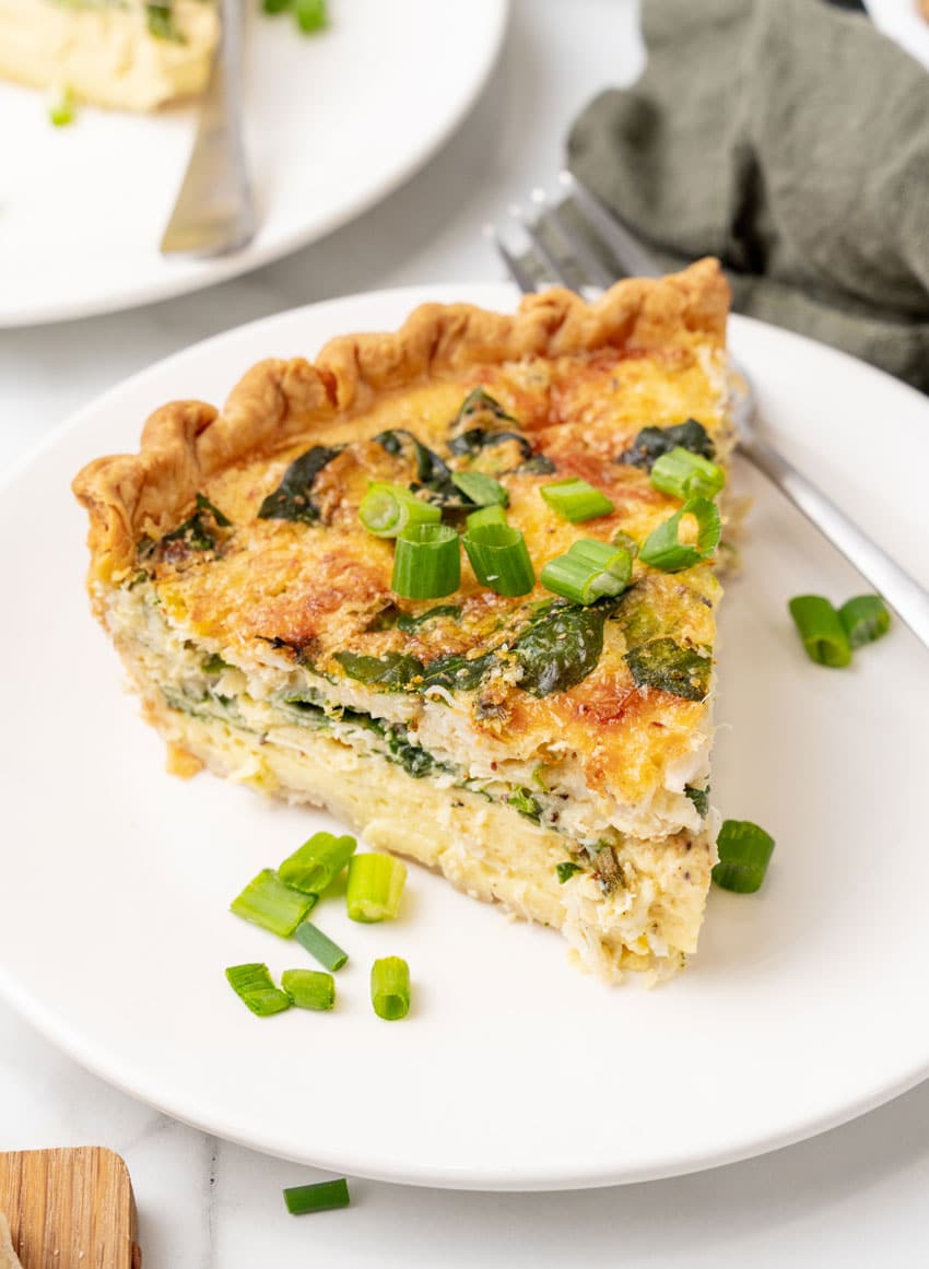 a slice of crab quiche on a small white plate with a silver fork resting on the side