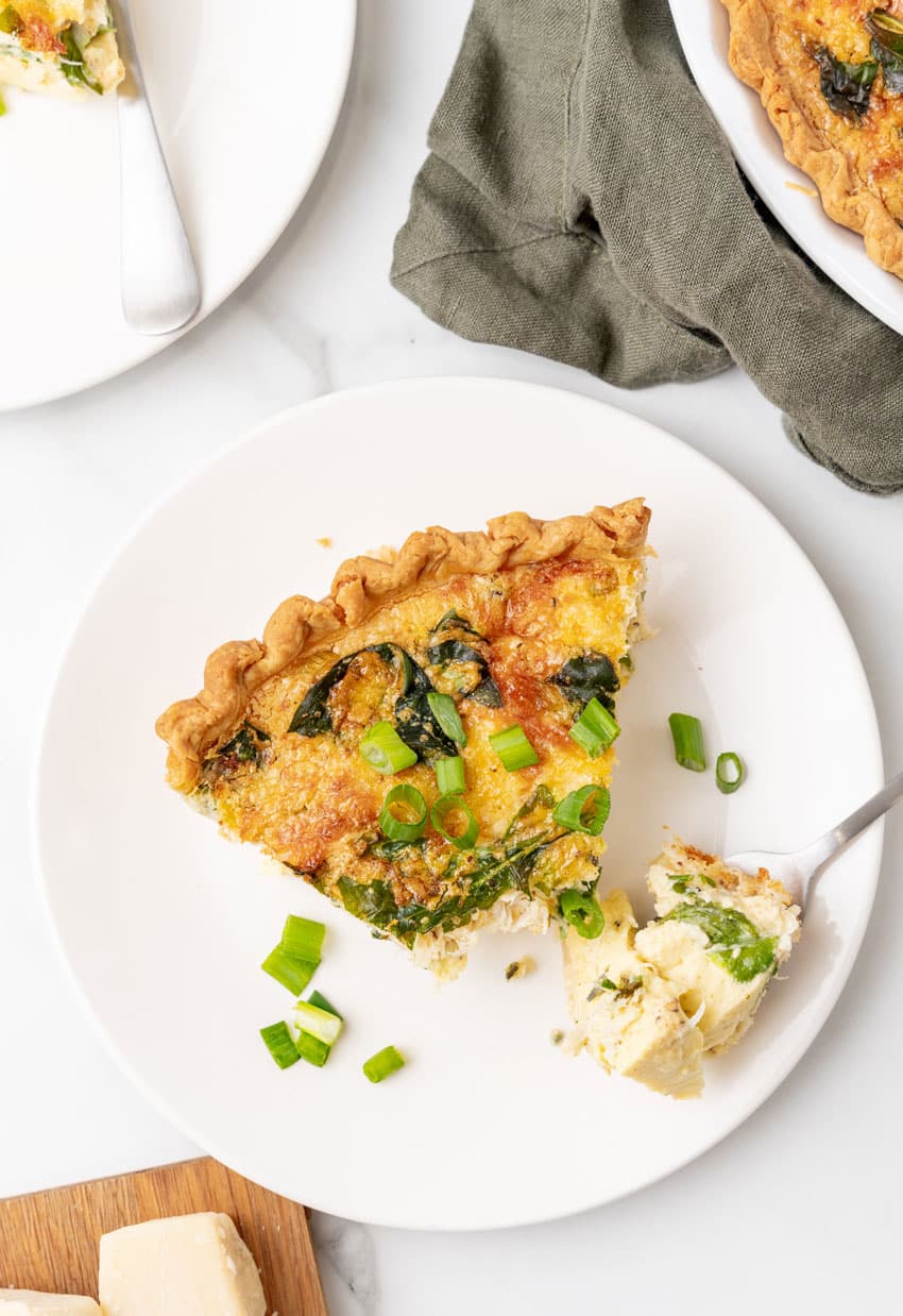 a slice of crab quiche on a small white plate with a silver fork resting on the side