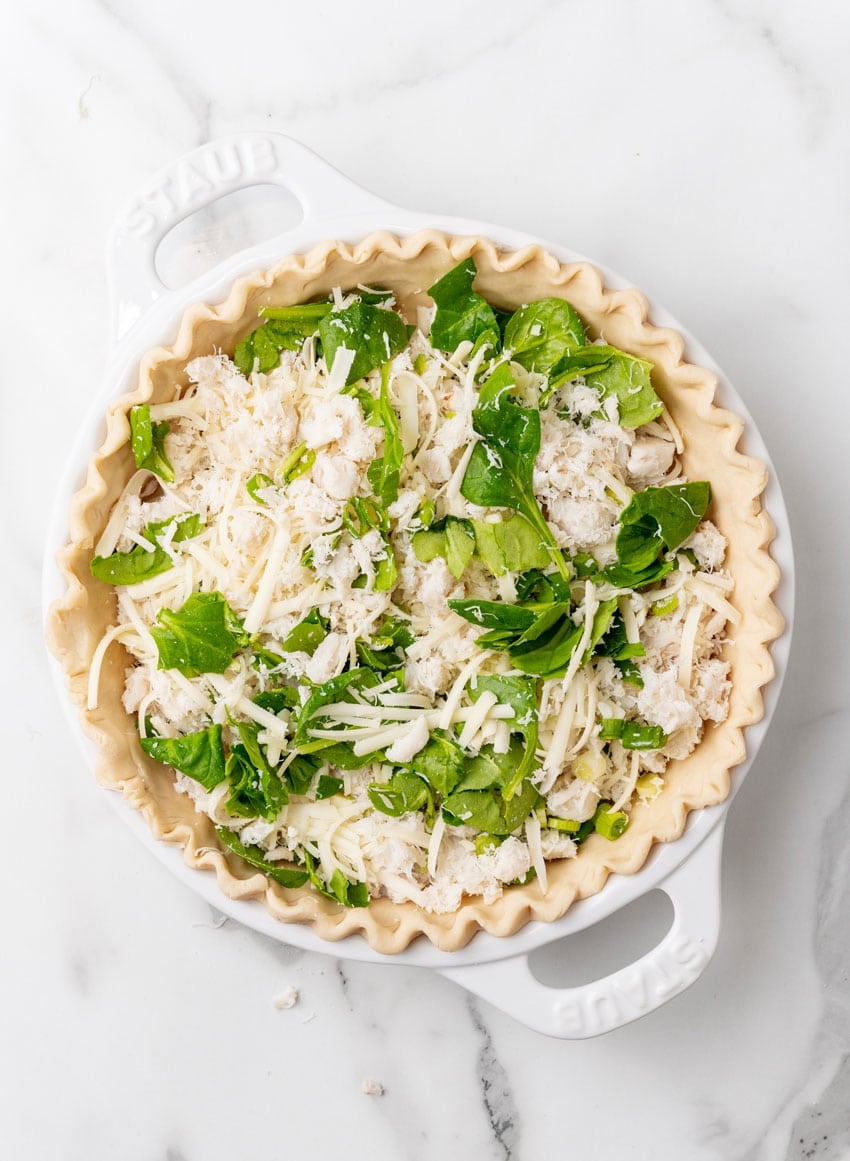 lump crab meat and fresh spinach spread out in an even layer in the bottom of a prepared pie crust