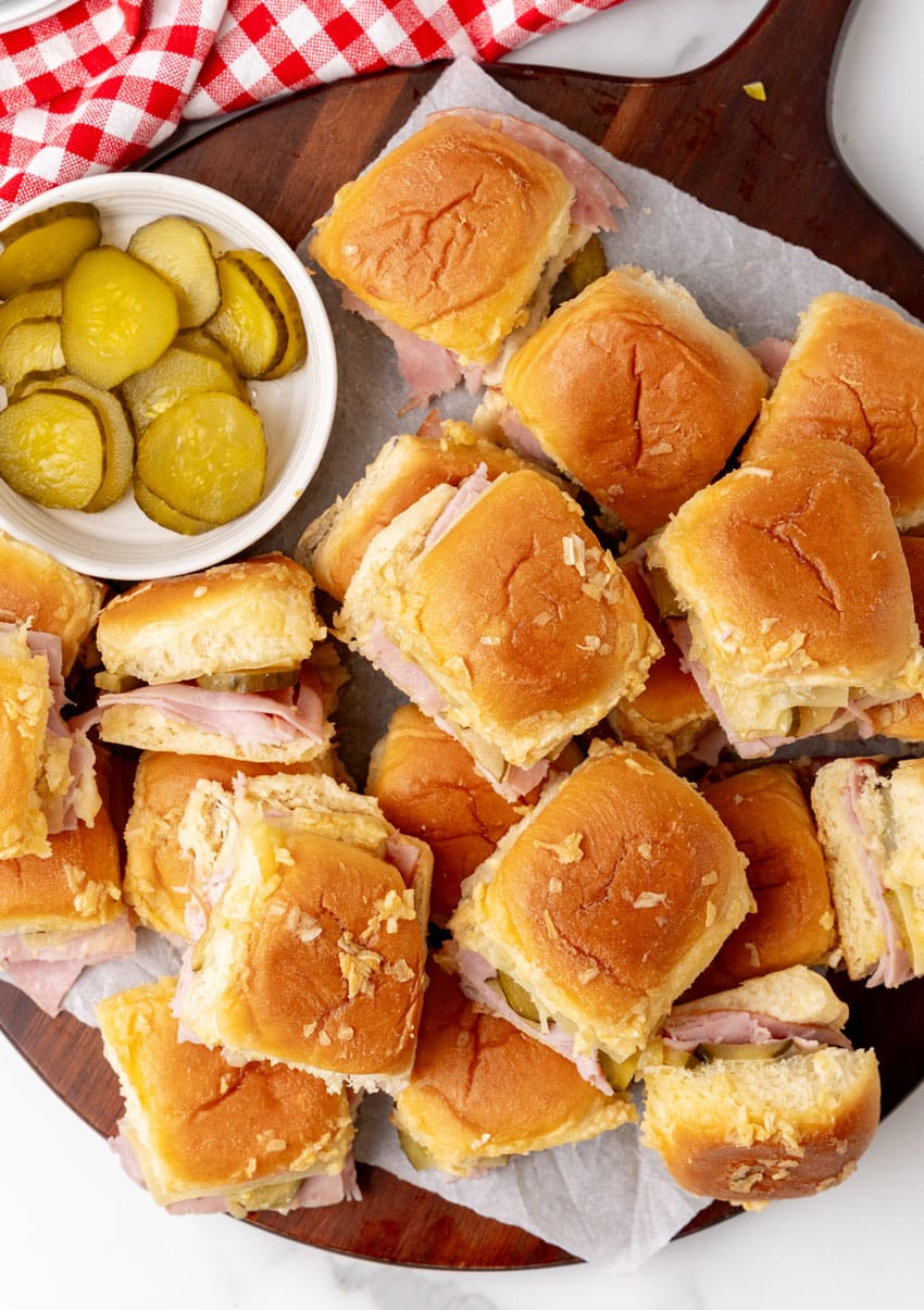 cuban style sliders on hawaiian rolls on a parchment paper lined wooden cutting board