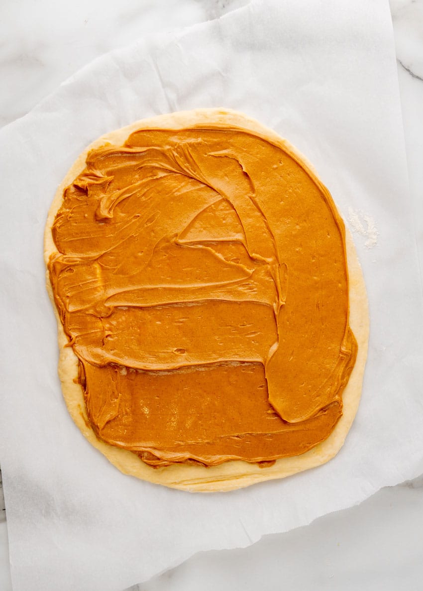 peanut butter spread over cinnamon roll dough on a white parchment paper