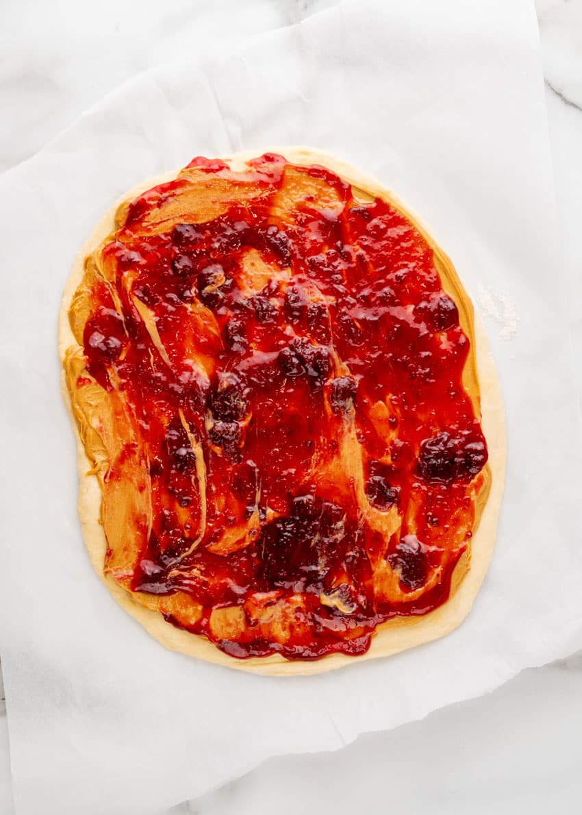 peanut butter and jelly spread over cinnamon roll dough on a white parchment paper