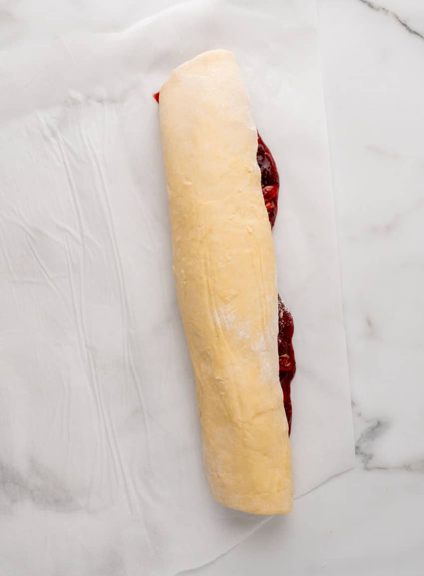 peanut butter and jelly filled sweet roll dough rolled up in a log and resting on white parchment paper