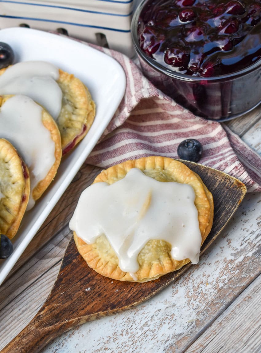a glazed air fryer blueberry hand pie  resting on a wooden spatula