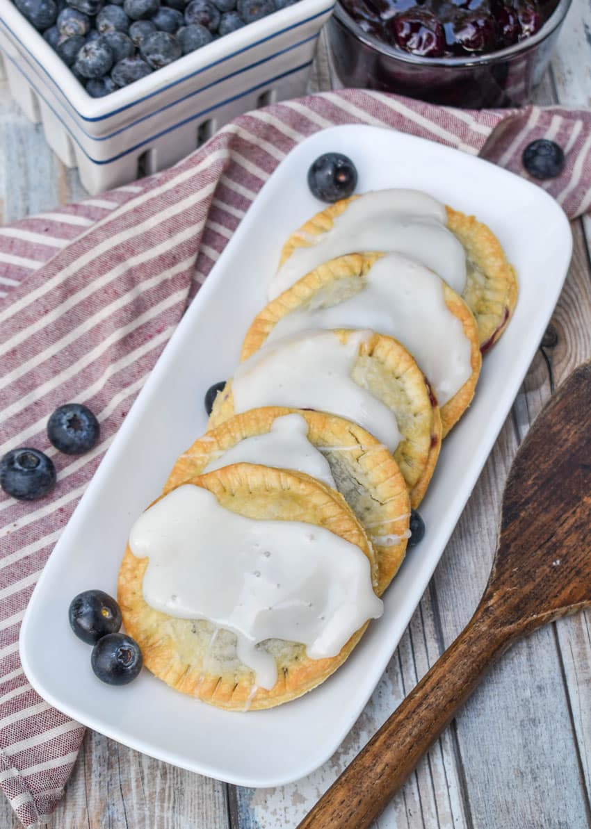air fryer blueberry hand pies arranged in a row on a narrow white serving dish with fresh blueberries on the side