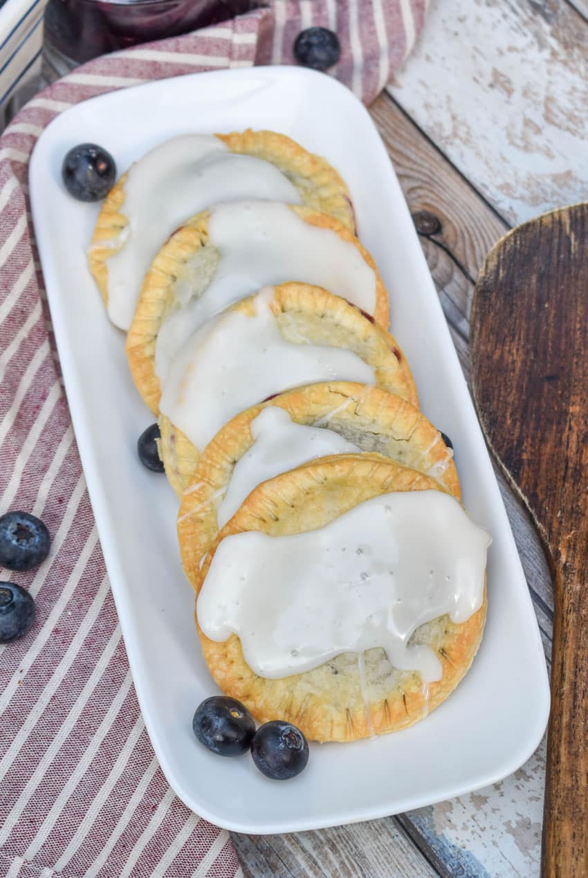air fryer blueberry hand pies arranged in a row on a narrow white serving dish with fresh blueberries on the side