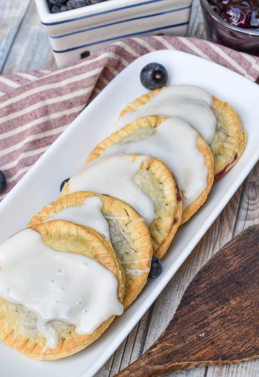 air fryer blueberry hand pies arranged in a row on a narrow white serving dish with fresh blueberries on the side