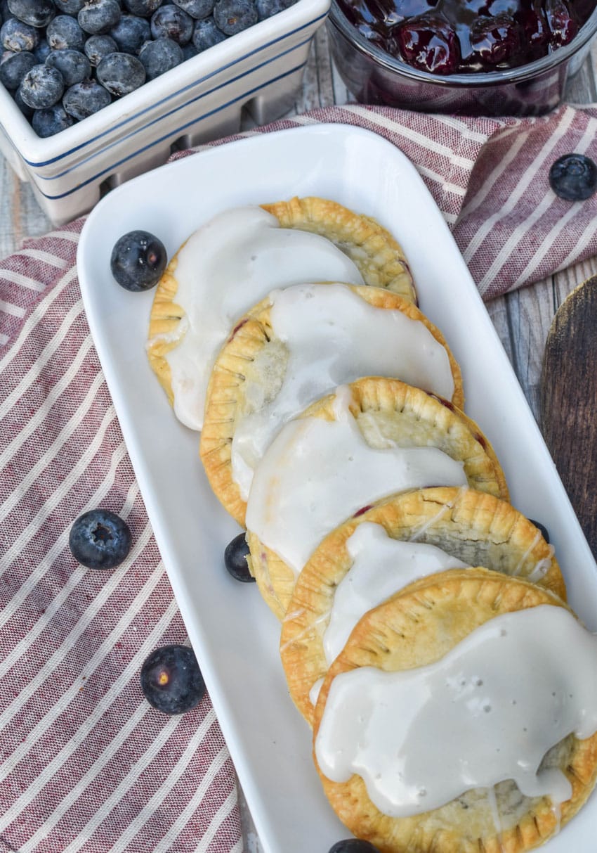 air fryer blueberry hand pies arranged in a row on a narrow white serving dish with fresh blueberries on the side