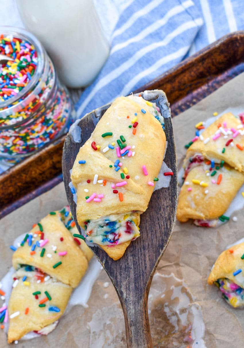 a wooden spatula lifting a funfetti cheesecake stuffed crescent roll off a parchment paper lined baking sheet