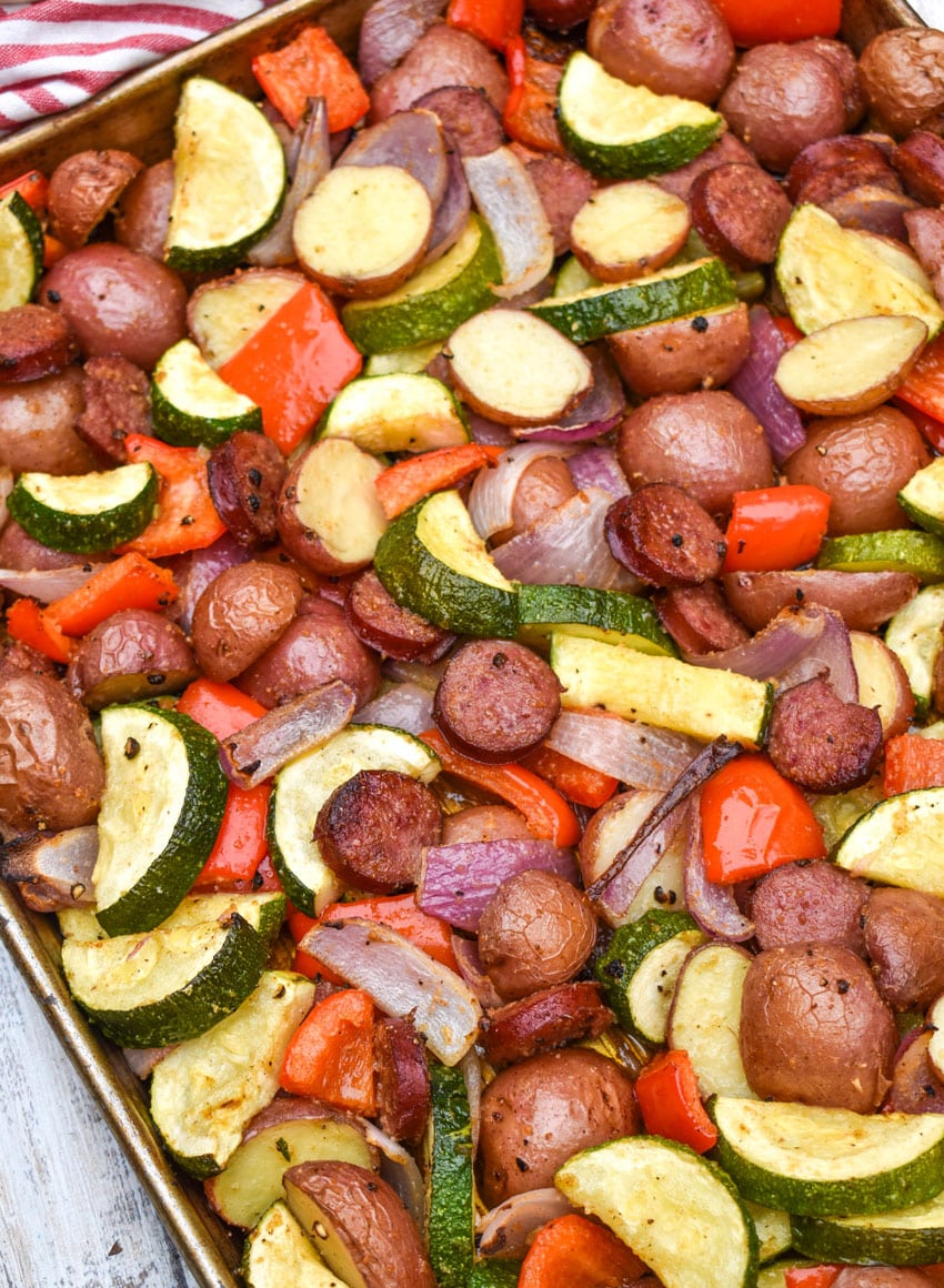 slices of kielbasa sausage and roasted vegetables on a metal sheet pan