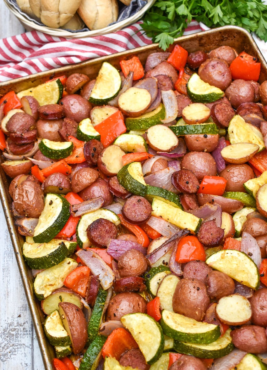 slices of kielbasa sausage and roasted vegetables on a metal sheet pan