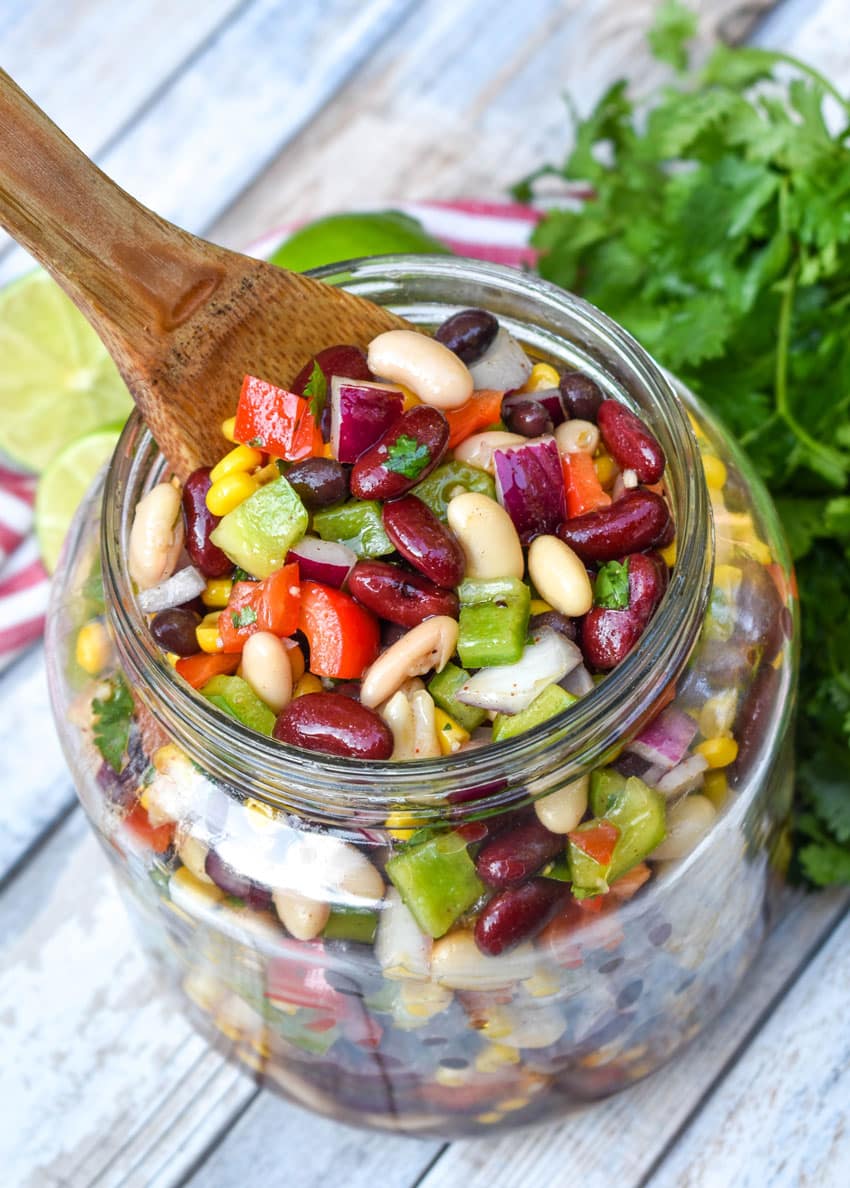 a wooden spoon scooping Mexican three bean salad out of a glass mason jar
