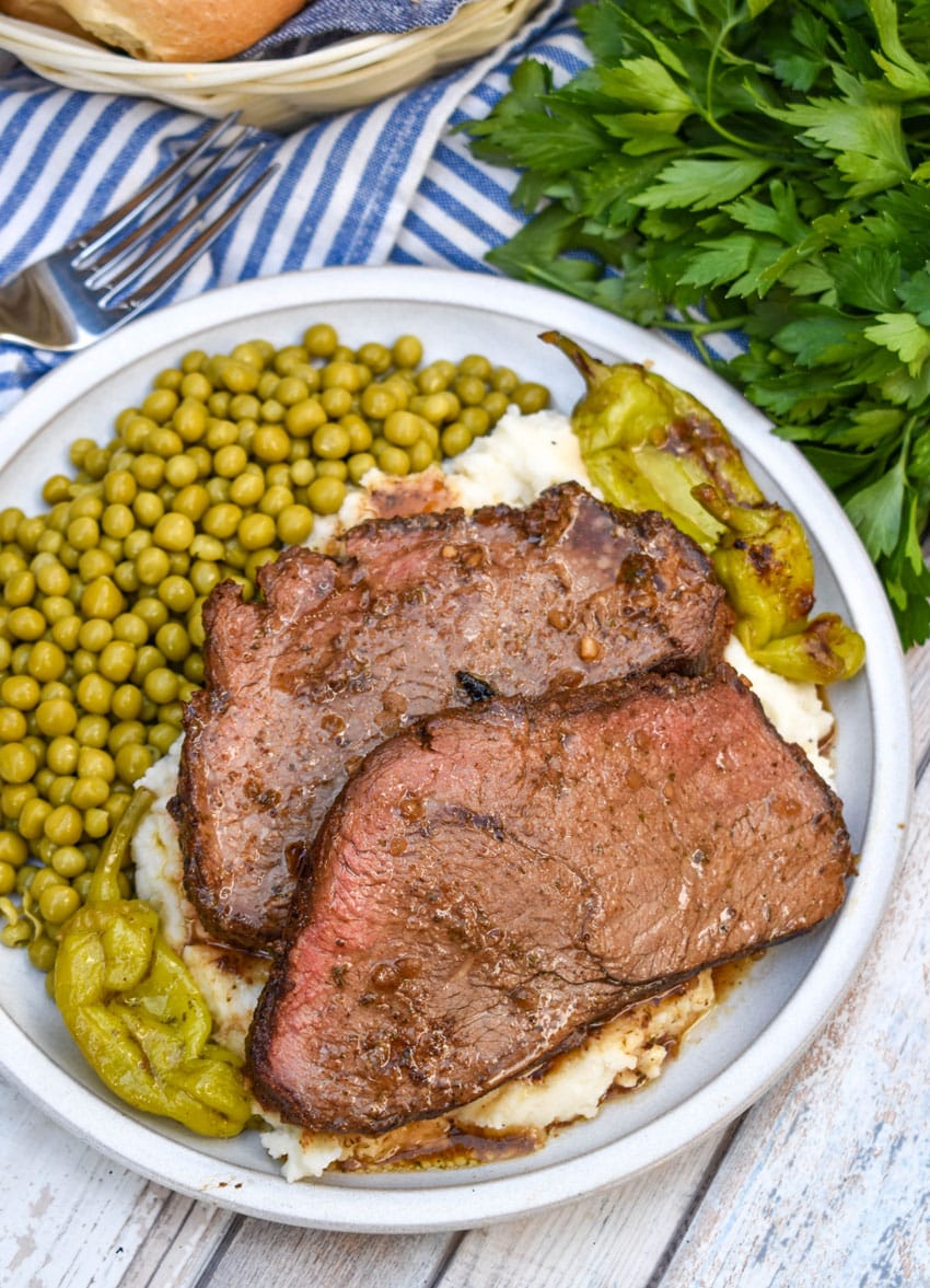 slices of smoked mississippi pot roast over mashed potatoes on a white plate