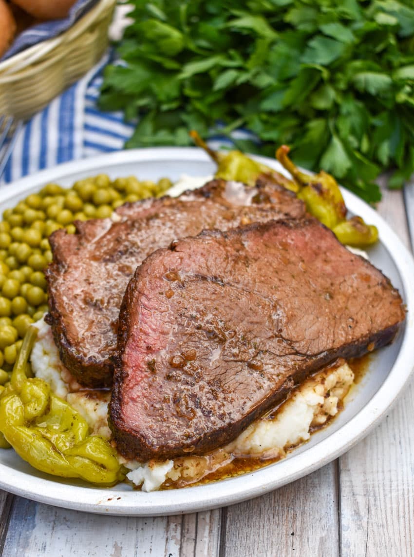slices of smoked mississippi pot roast over mashed potatoes on a white plate