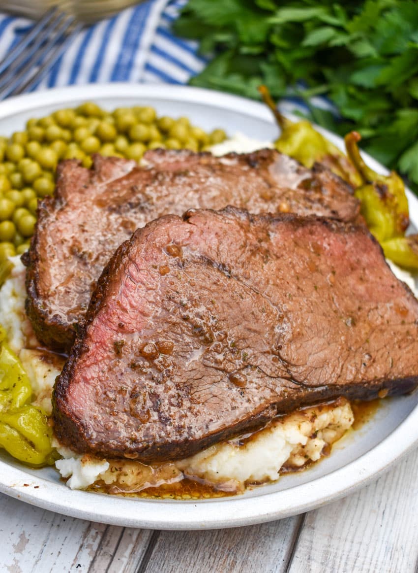 slices of smoked mississippi pot roast over mashed potatoes on a white plate