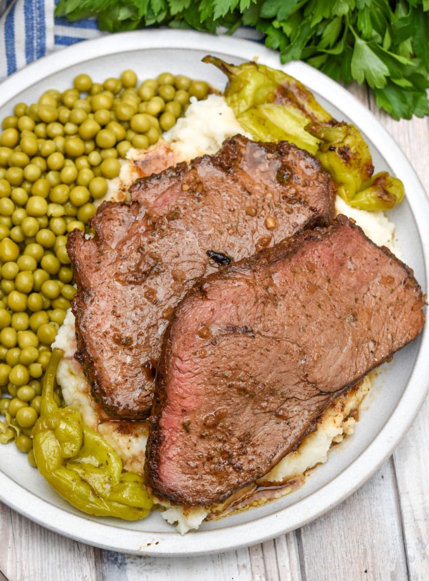 slices of smoked mississippi pot roast over mashed potatoes on a white plate