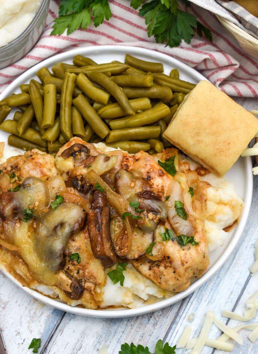 copycat texas roadhouse smothered chicken over mashed potatoes with green beans on the side on a white plate