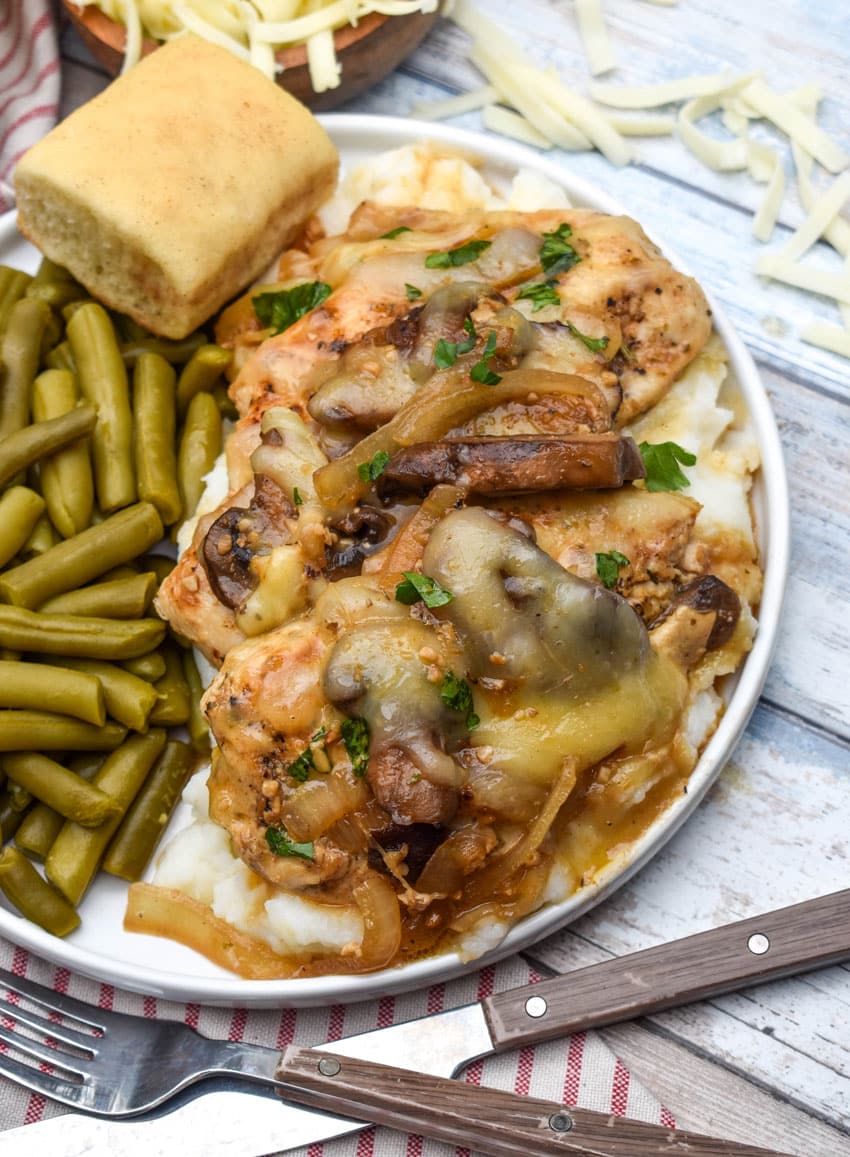 copycat texas roadhouse smothered chicken over mashed potatoes with green beans on the side on a white plate