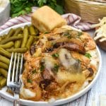 copycat texas roadhouse smothered chicken over mashed potatoes with green beans on the side on a white plate