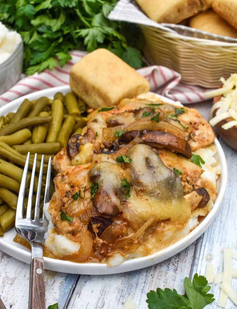 copycat texas roadhouse smothered chicken over mashed potatoes with green beans on the side on a white plate