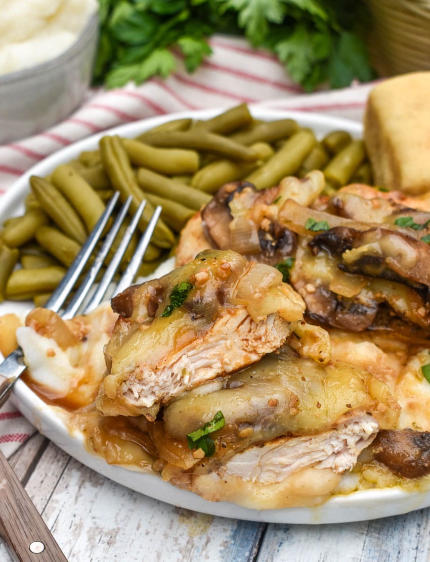 copycat texas roadhouse smothered chicken over mashed potatoes with green beans on the side on a white plate