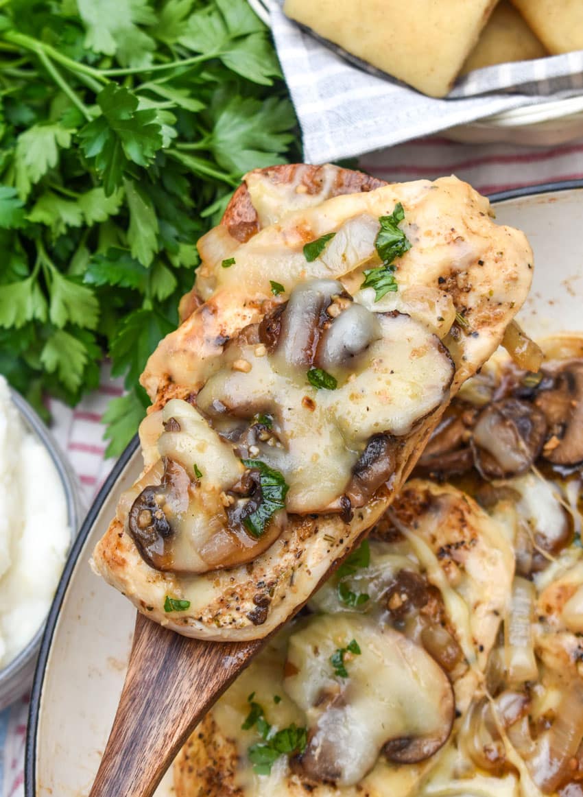 a wooden spatula holding up a copycat cheesy smothered chicken breast