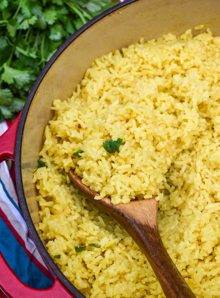 a wooden spoon scooping homemade yellow rice out of a large dutch oven