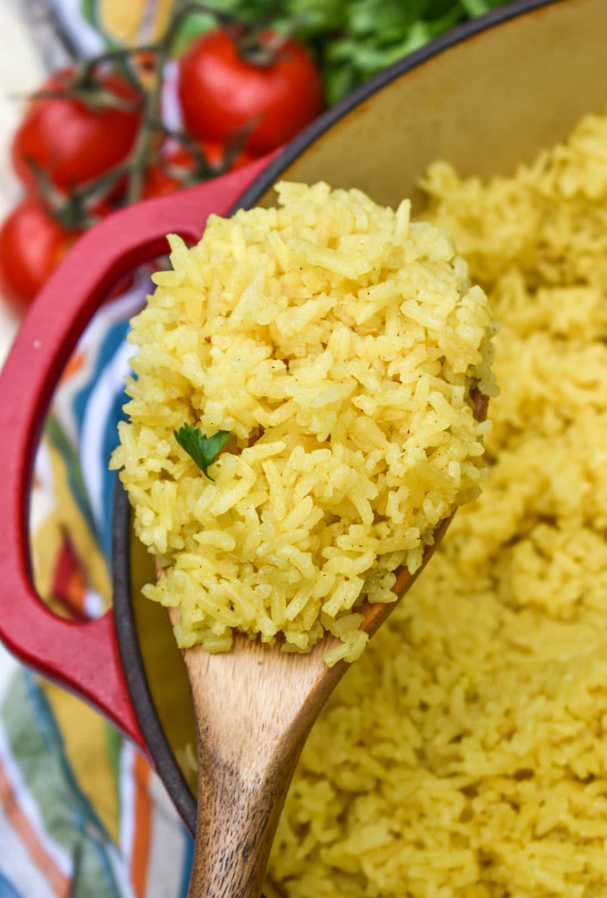 a wooden spoon holding up a scoop of homemade yellow rice