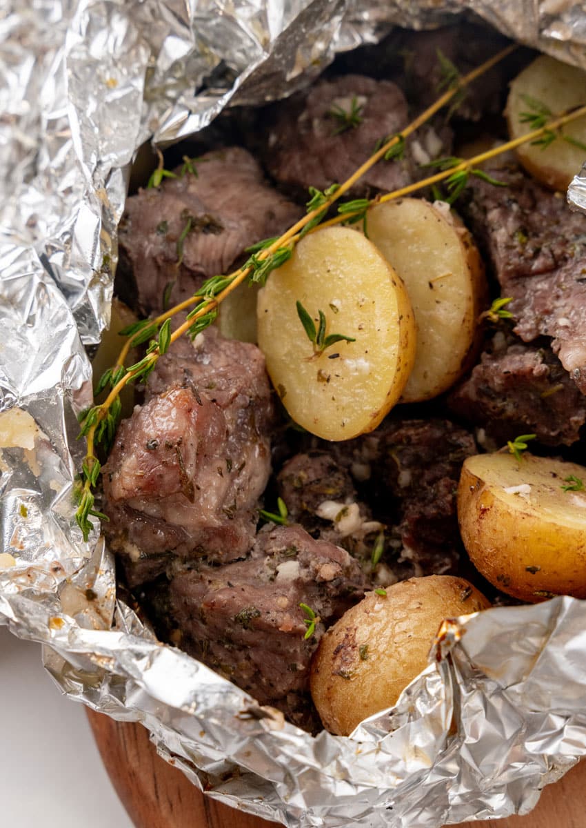 an opened garlic butter grilled steal and potato foil packet resting on a wooden cutting board